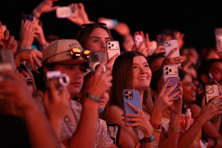 A group of fans all with their phones up listen to a band at a concert.