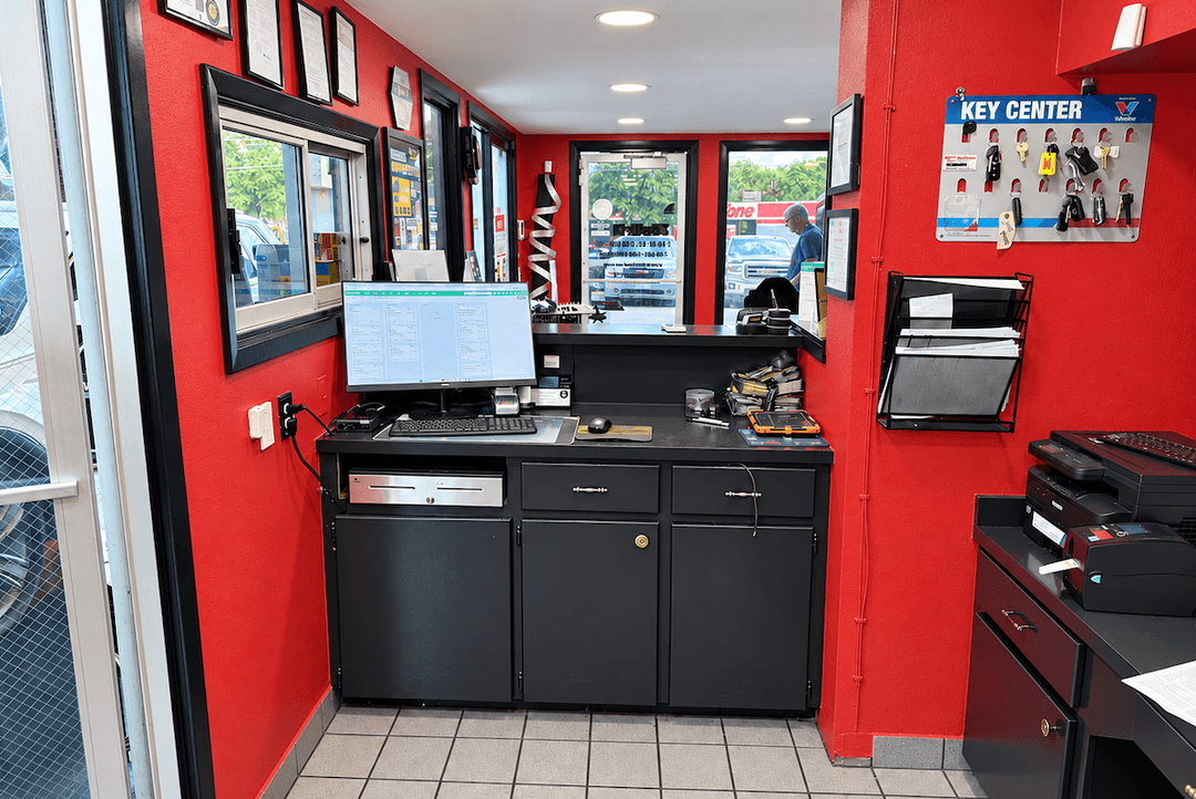 Auto shop front desk with red walls, computer, cash drawer, and Key Center display board on wall.