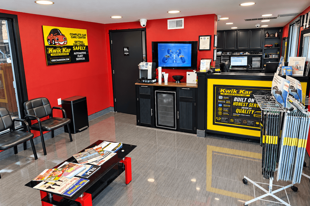 Kwik Kar auto care waiting room with red walls, black chairs, magazine table, service counter and coffee station.
