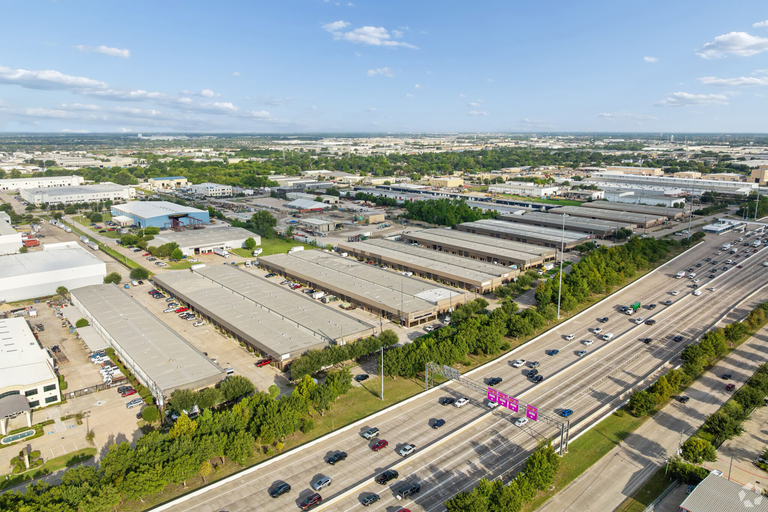 Aerial view of an industrial area with warehouses alongside a busy multi-lane highway under a clear blue sky.
