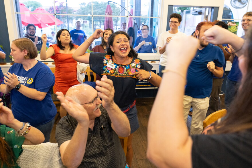 A woman with arms in the air celebrates with others at an election night party.
