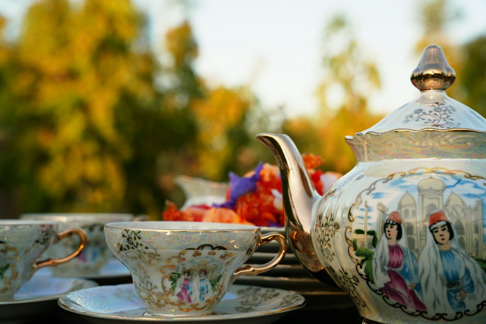 A porcelain teapot and teacups with painted figures in a sunlit garden