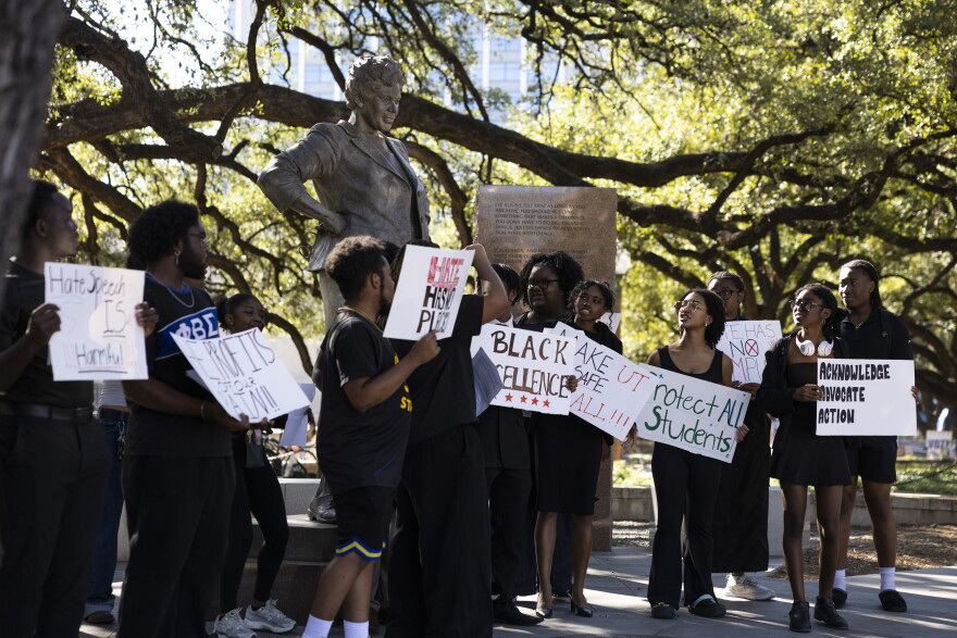 A group of students hold protest signs in front of a statue of Barbara Jordan. 