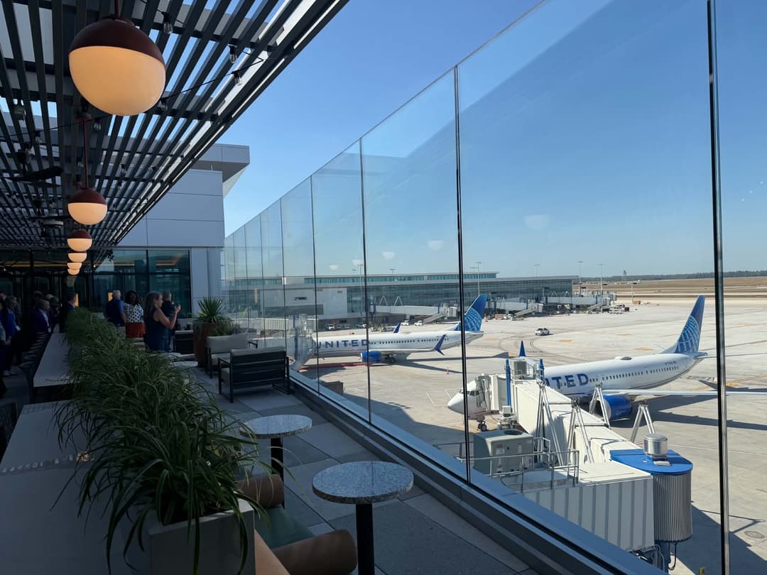 View from airport terminal lounge of United Airlines jets parked at gates under clear blue sky.