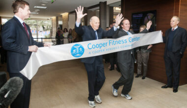 Former Dallas Cowboys quarterbacks Troy Aikman (left) and Roger Staubach hold a banner for Dr. Kenneth Cooper and his son, Dr. Tyler Cooper, to run through during the unveiling of the Cooper Fitness Center's new 50,000-square-foot expansion.