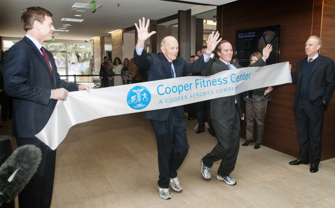 Former Dallas Cowboys quarterbacks Troy Aikman (left) and Roger Staubach hold a banner for Dr. Kenneth Cooper and his son, Dr. Tyler Cooper, to run through during the unveiling of the Cooper Fitness Center's new 50,000-square-foot expansion.