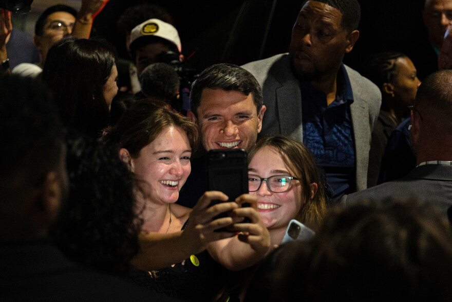 A man poses for a cell phone photo with two women.