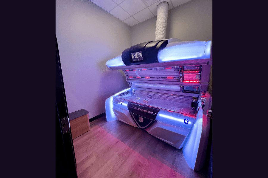 Open tanning bed with blue and red lights in a small room with wood flooring.