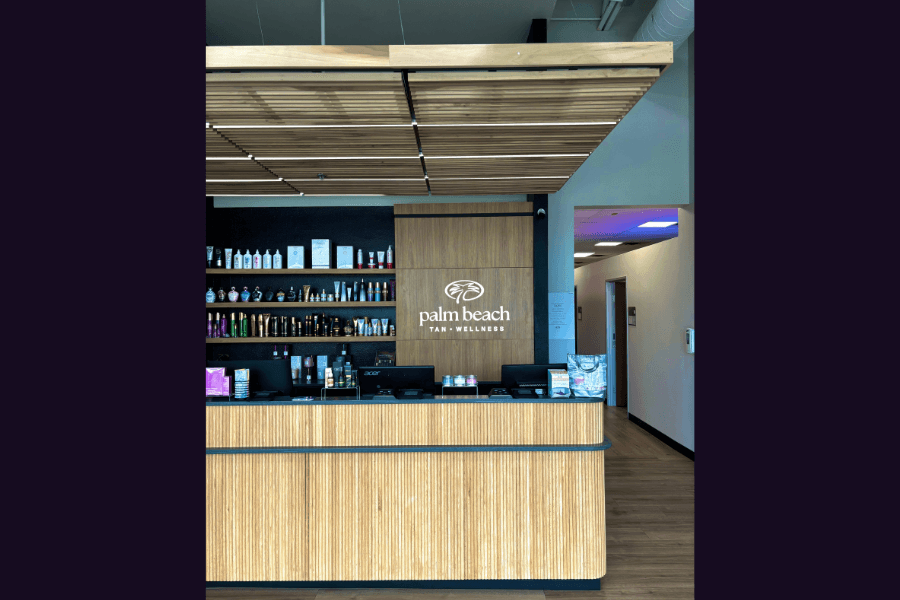 Palm Beach Tan Wellness reception desk with wood paneling and shelves of tanning products behind.