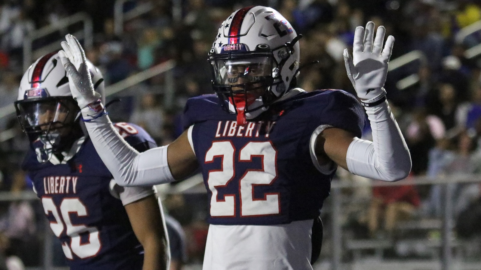 Liberty football player #22 raises arms in celebration on the field during a game, nighttime stadium in background