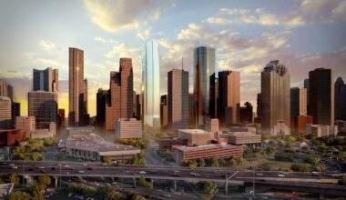A city skyline at sunset featuring tall skyscrapers, highways with traffic, and scattered clouds in the sky.