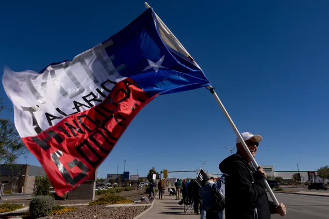 A participant carries a Texas flag with political messages along Eastlake Boulevard during a “No Kings” sidewalk protest organized by Indivisible the 915 in El Paso, Texas, on Saturday, Oct. 17, 2026.