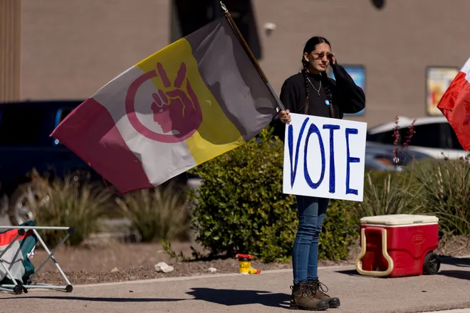 A participant holds a “Vote” sign and a flag during a “No Kings” sidewalk protest organized by Indivisible the 915 along Eastlake Boulevard in El Paso, Texas, on Saturday, Oct. 17, 2026.
