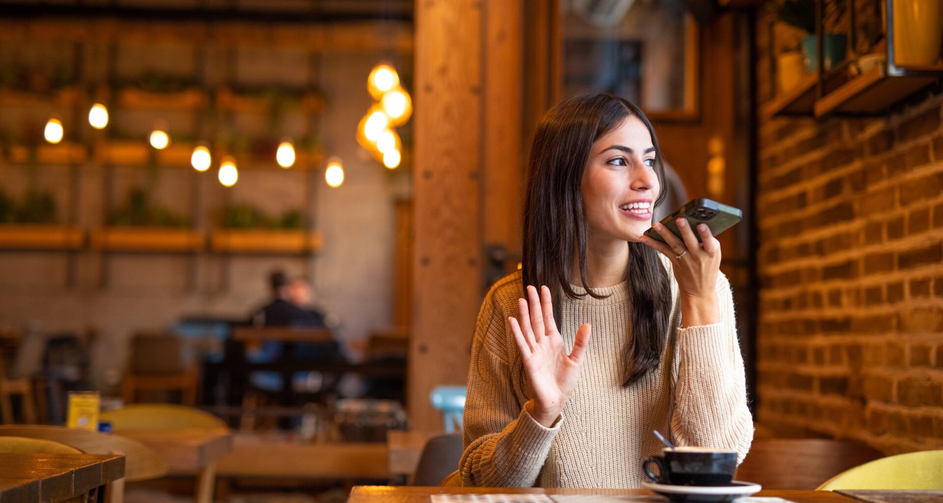 a woman sitting at a restaurant table talking on a speaker phone.