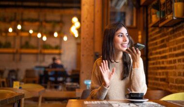 a woman sitting at a restaurant table talking on a speaker phone.