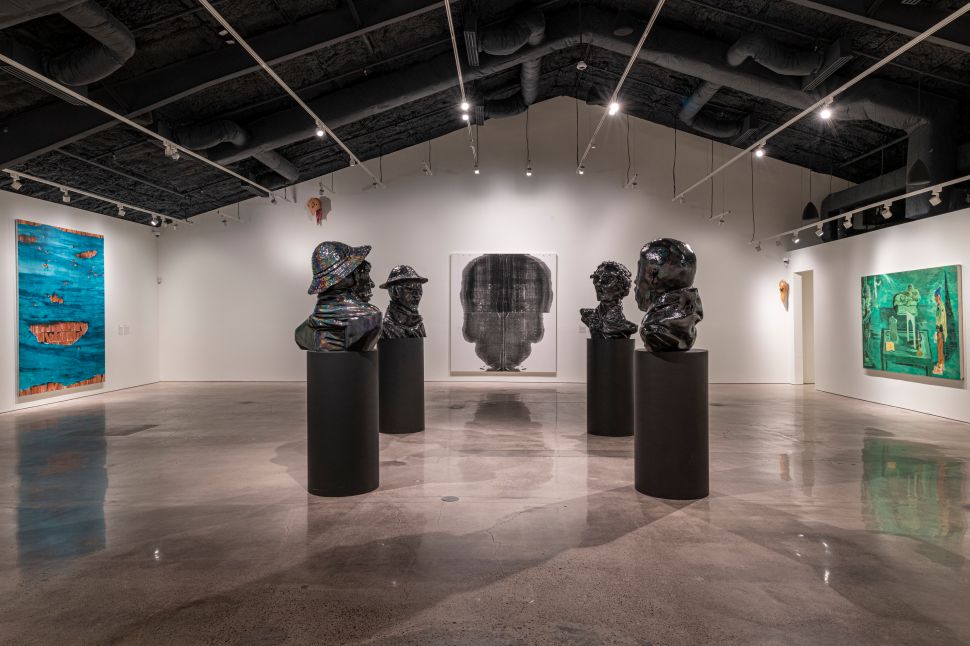 A spacious installation view of Ostillo Art Foundation in Austin, with sculptural busts on black pedestals and contemporary artworks displayed across white gallery walls.
