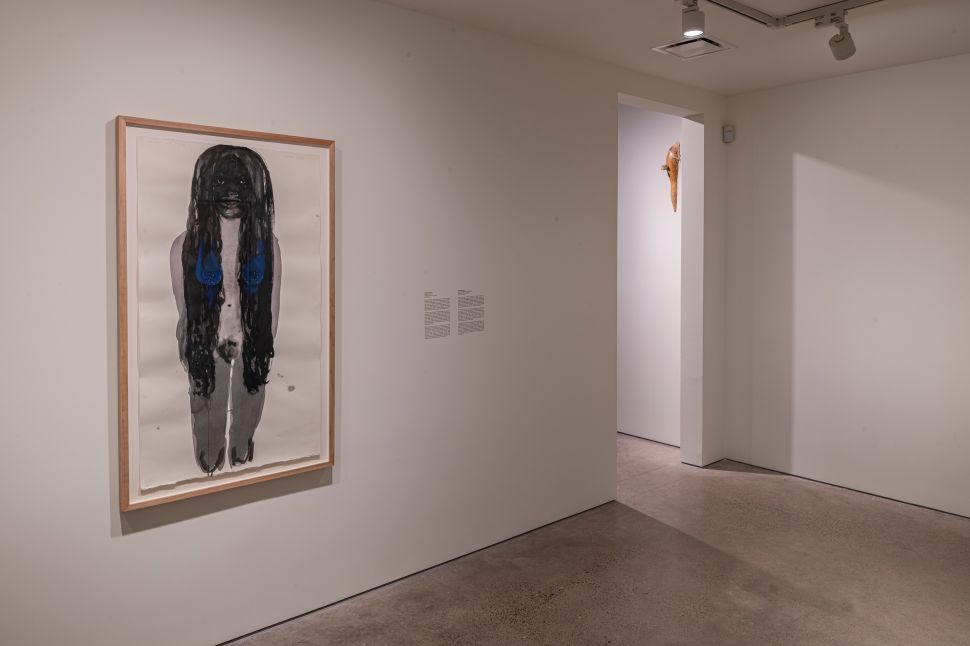 A framed figurative work with a dark, elongated human form and blue accents hangs in a quiet gallery passage at Ostillo Art Foundation.