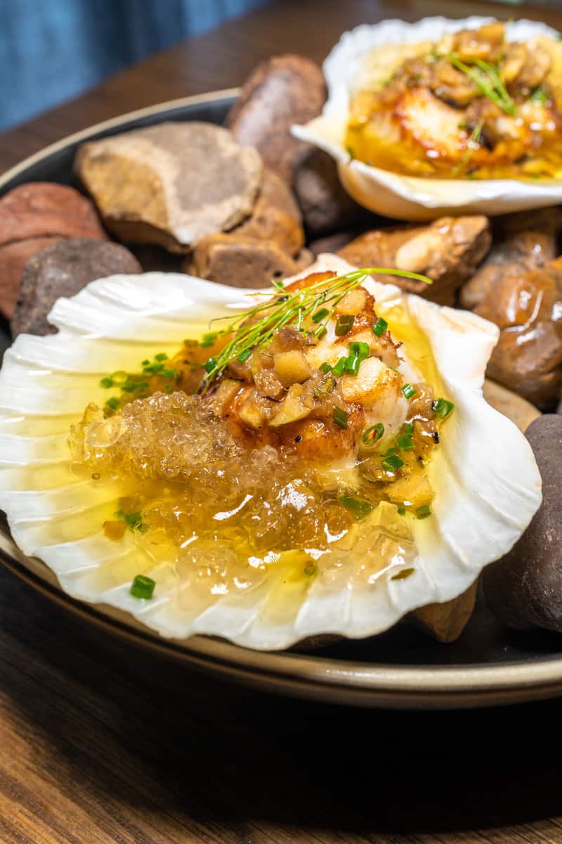 Gourmet scallops topped with sauce and garnish, surrounded by stones in a bowl.