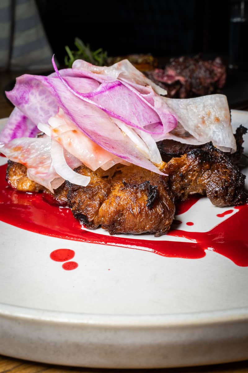 Grilled meat topped with pickled onions on a plate with red sauce.