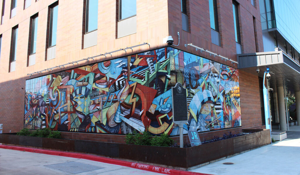 A colorful abstract graffiti mural covers a brick building corner, featuring bold geometric shapes and figures.
