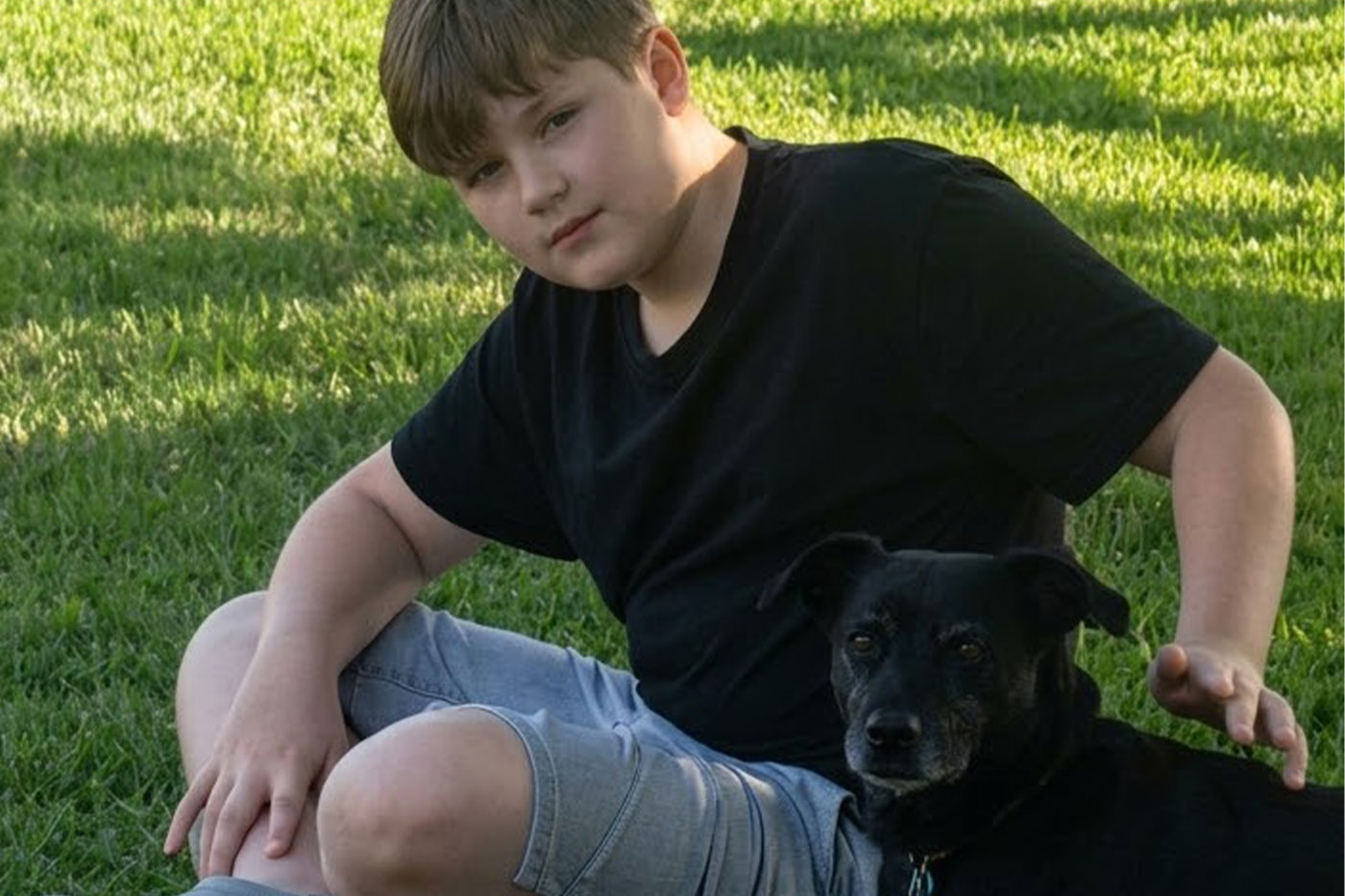 Ty isits on the grass with his small black rescue dog.