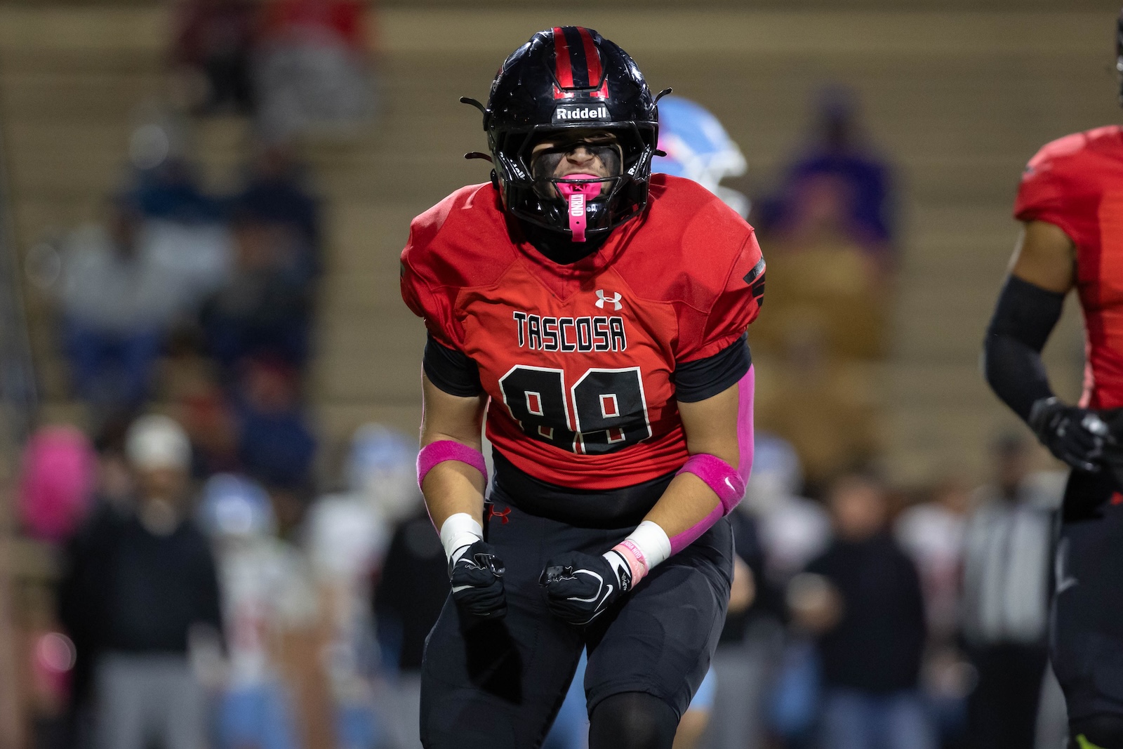 MHS-THS-FB-17 | Press Pass Sports Football player in a red jersey with the number 98 rushing toward the camera, wearing a black helmet with pink accents and pink arm bands, on a crowded indoor field.