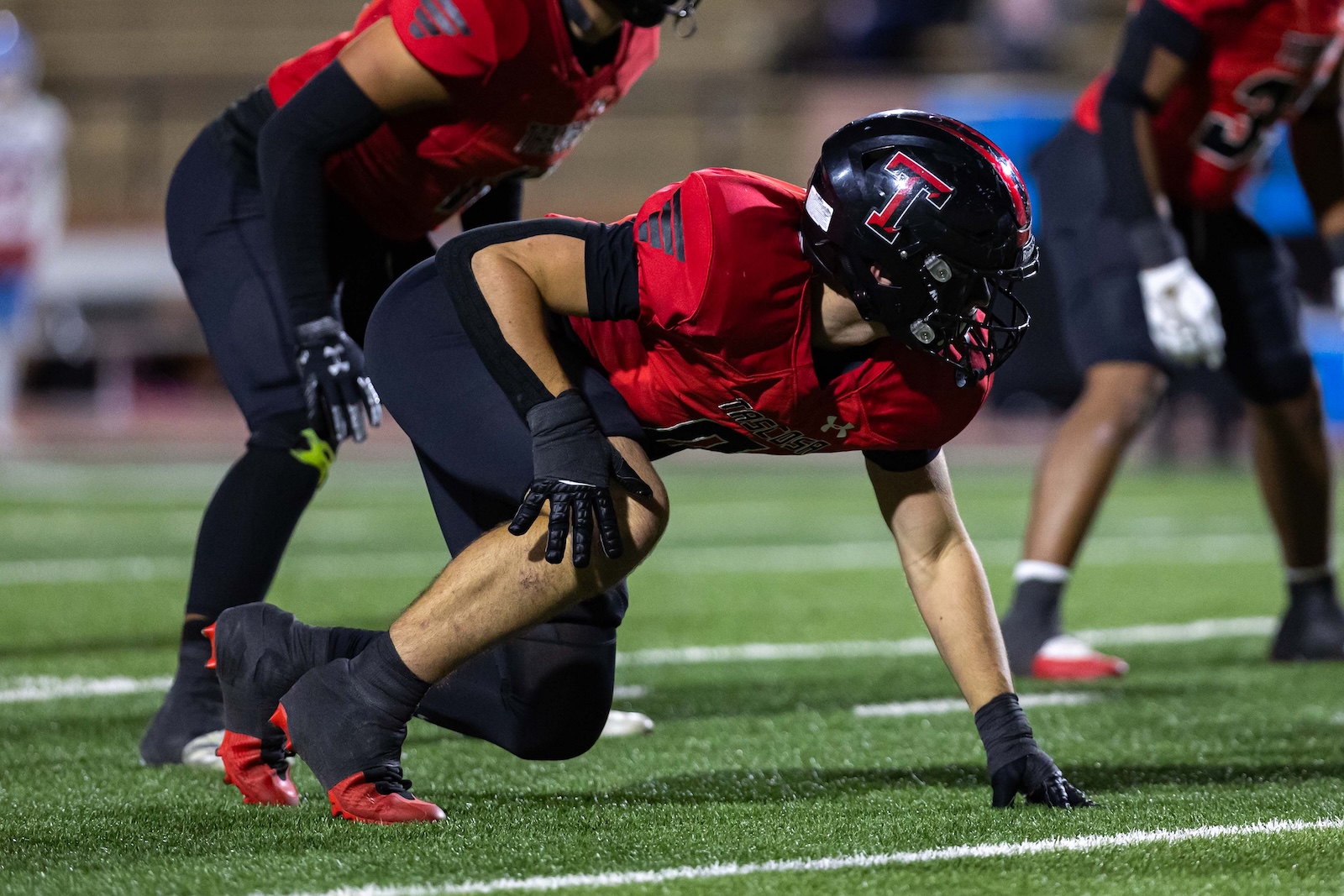 MHS-THS-FB-37 | Press Pass Sports Two football linemen in red jerseys crouch on a grassy turf field, ready for the snap.