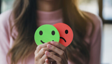 Woman Hands holding sad face hiding or behind happy smiley face, bipolar and depression, mental health concept, personality, mood change, therapy healing split concept.