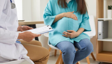 pregnant woman sitting at the desk in doctor's office visiting clinic. Health provider holding report file and giving consultation during medical exam