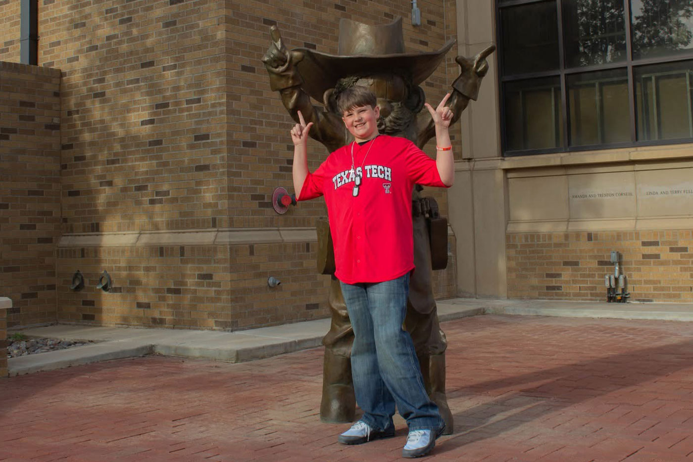 Ty poses with his guns up in front of a statue of Raider Red outside the Frazier Alumni Pavilion.