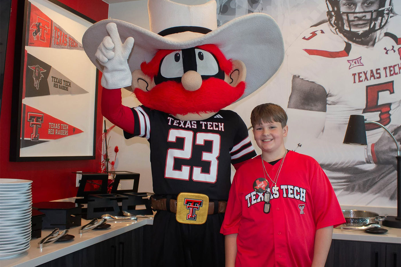 Ty wears a red Texas Tech shirt and poses beside Raider Red at Raider Nation Day.