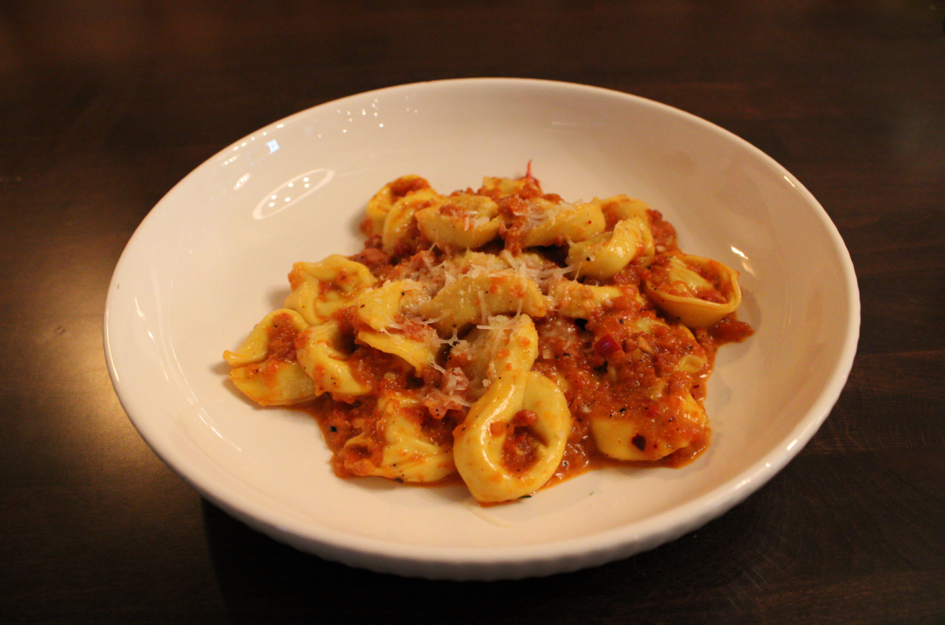 A bowl of Sorella's tortellini alla niavola, with a bright red chili sauce and grated parmigiano reggiano