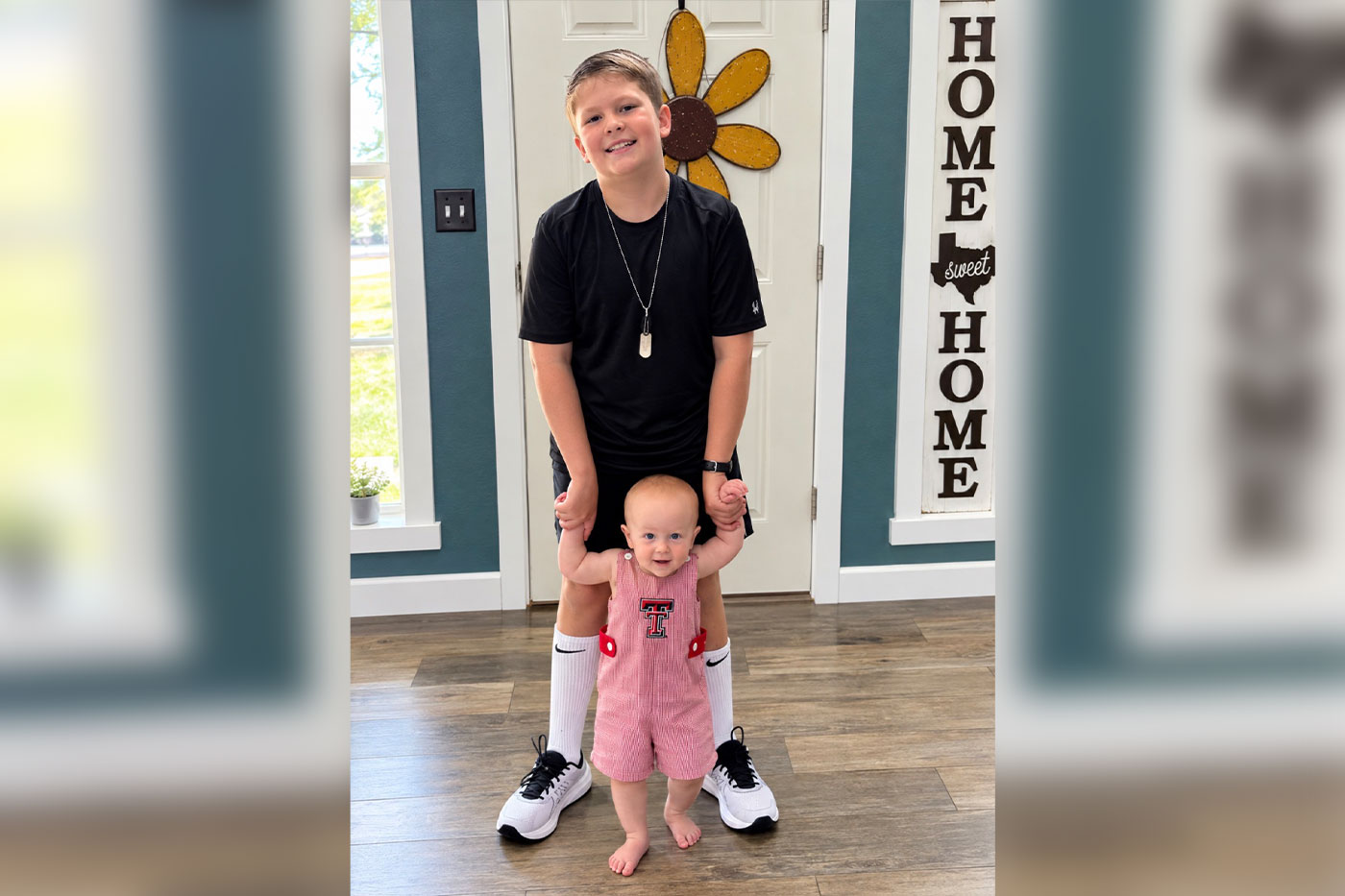 Ty stands behind his little brother, holding his hands to help him walk.