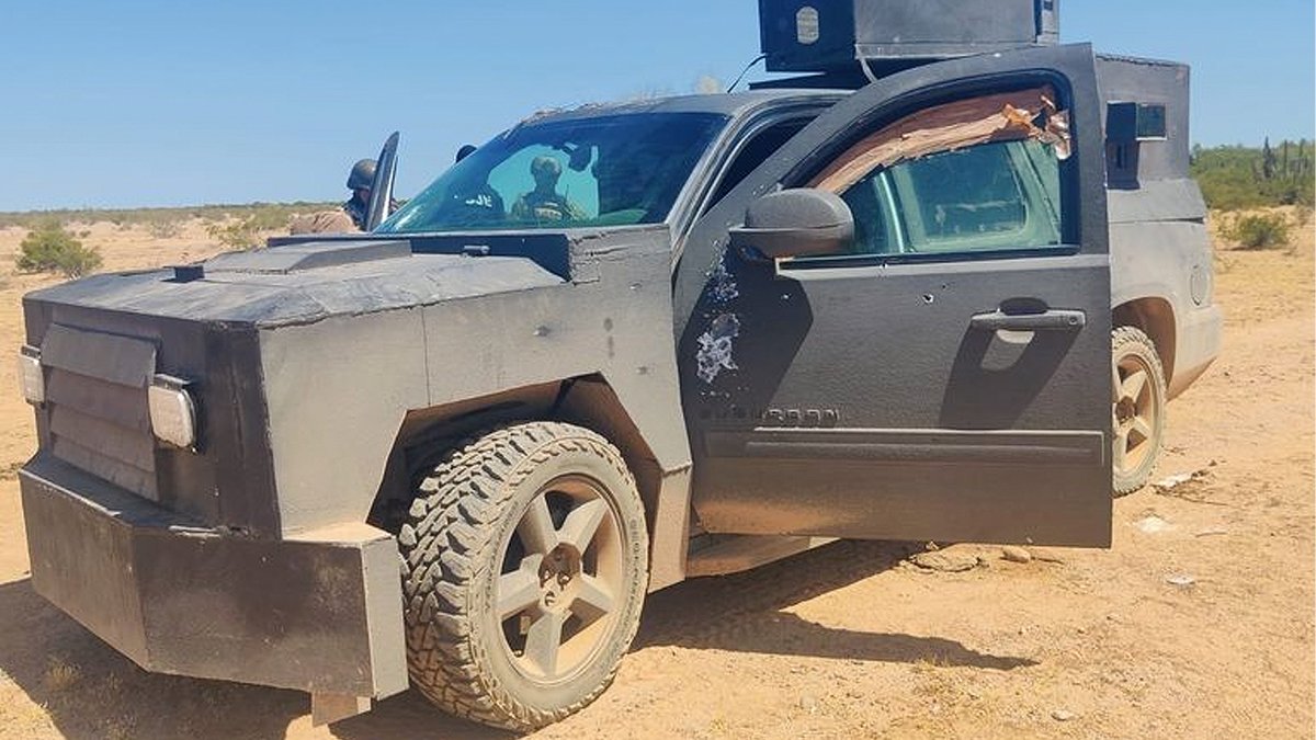 An armored black SUV sits on a dirt road with its driver’s door open