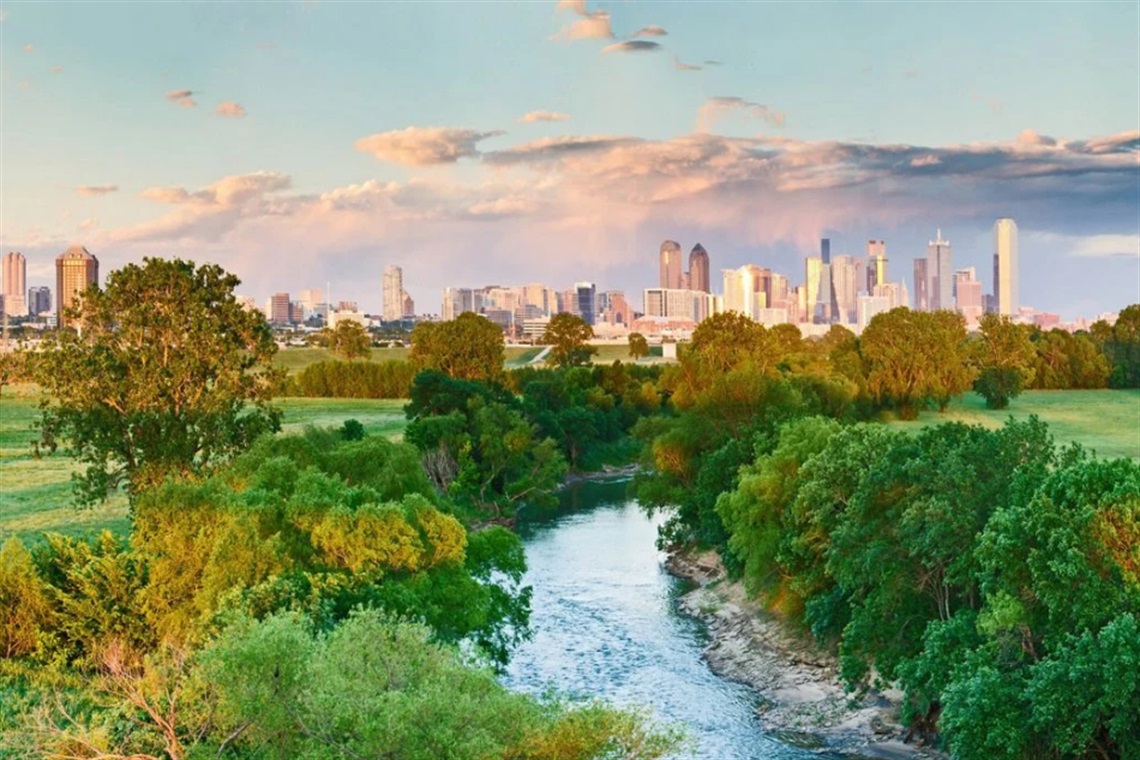 Aerial image of a tree-lined creek flowing near the Dallas city skyline.