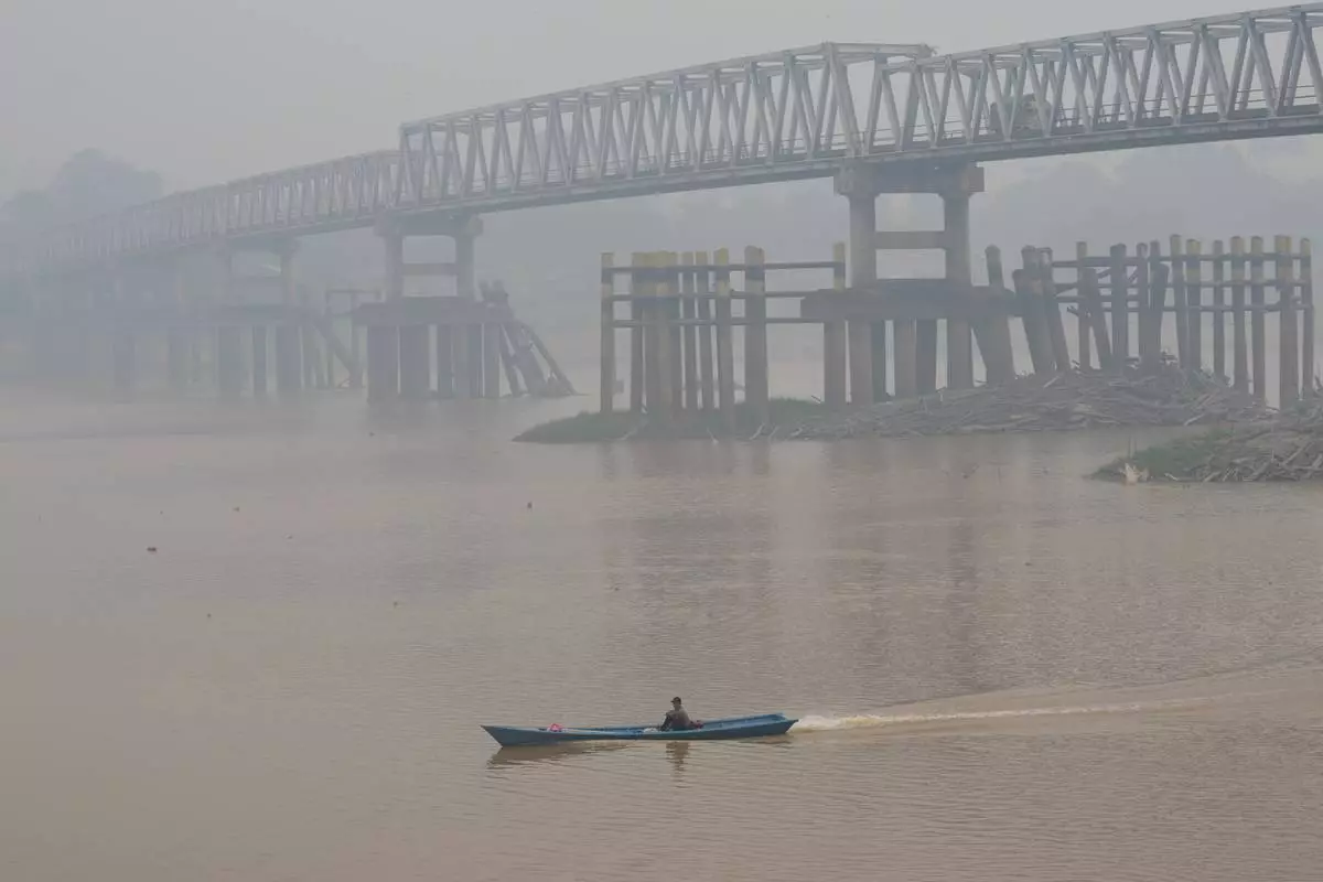 A man pilots a motorboat along the Kapuas River as a bridge is obscured by haze in Sekadau, West Kalimantan, Indonesia, Friday, Sept. 11, 2026. (AP Photo/Tatan Syuflana)