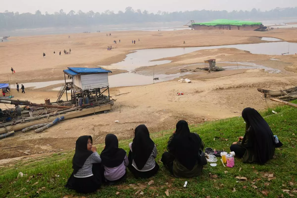 People look at a barge, back right, stranded on a dry riverbed of the Kapuas River amid a drought in Sekadau, West Kalimantan, Indonesia, Friday, Sept. 11, 2026. (AP Photo/Tatan Syuflana)