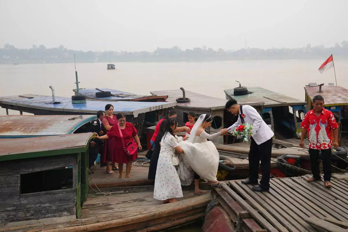 A groom helps a bride step between boats on the Kapuas River amid haze in Sekadau, West Kalimantan, Indonesia, Saturday, Sept. 12, 2026. (AP Photo/Tatan Syuflana)