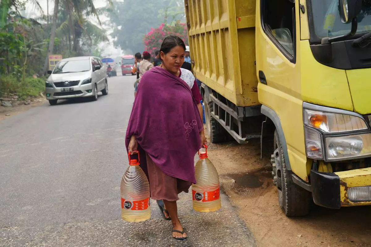 Sriwati, a shopkeeper and mother, carries two containers filled with clean water during a drought in Sanggau, West Kalimantan, Indonesia, Friday, Sept. 11, 2026. (AP Photo/Tatan Syuflana)