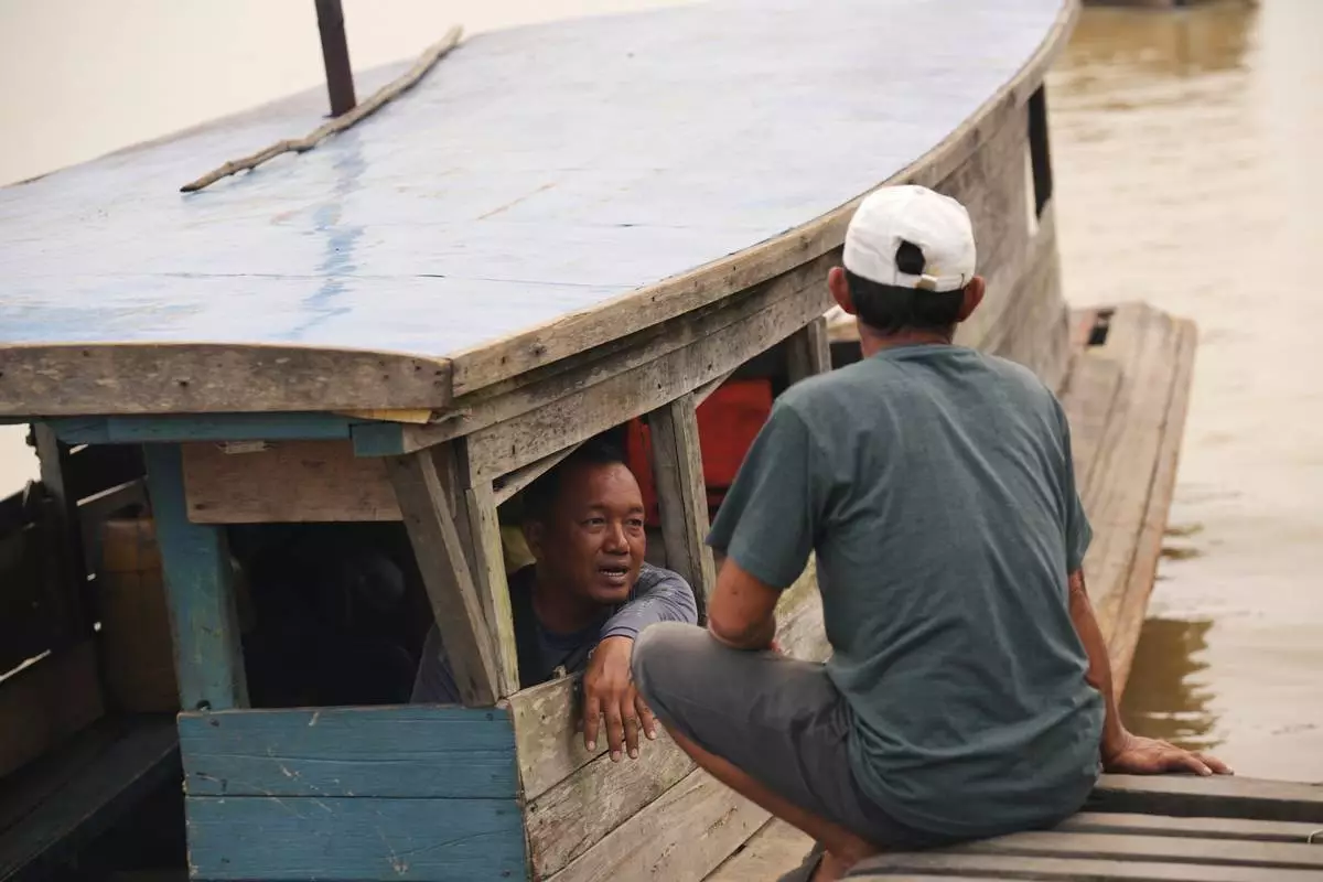 Abiansah, a boat operator, left, talks with a man at a wooden dock along the Kapuas River amid haze in Sekadau, West Kalimantan, Indonesia, Saturday, Sept. 12, 2026. (AP Photo/Tatan Syuflana)
