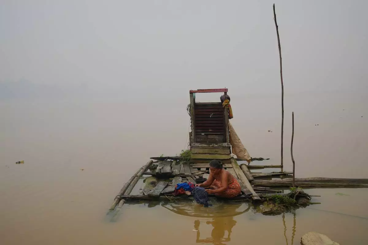 A woman washes clothes on a floating wooden platform along the Kapuas River amid haze in Sanggau, West Kalimantan, Indonesia, Friday, Sept. 11, 2026. (AP Photo/Tatan Syuflana)