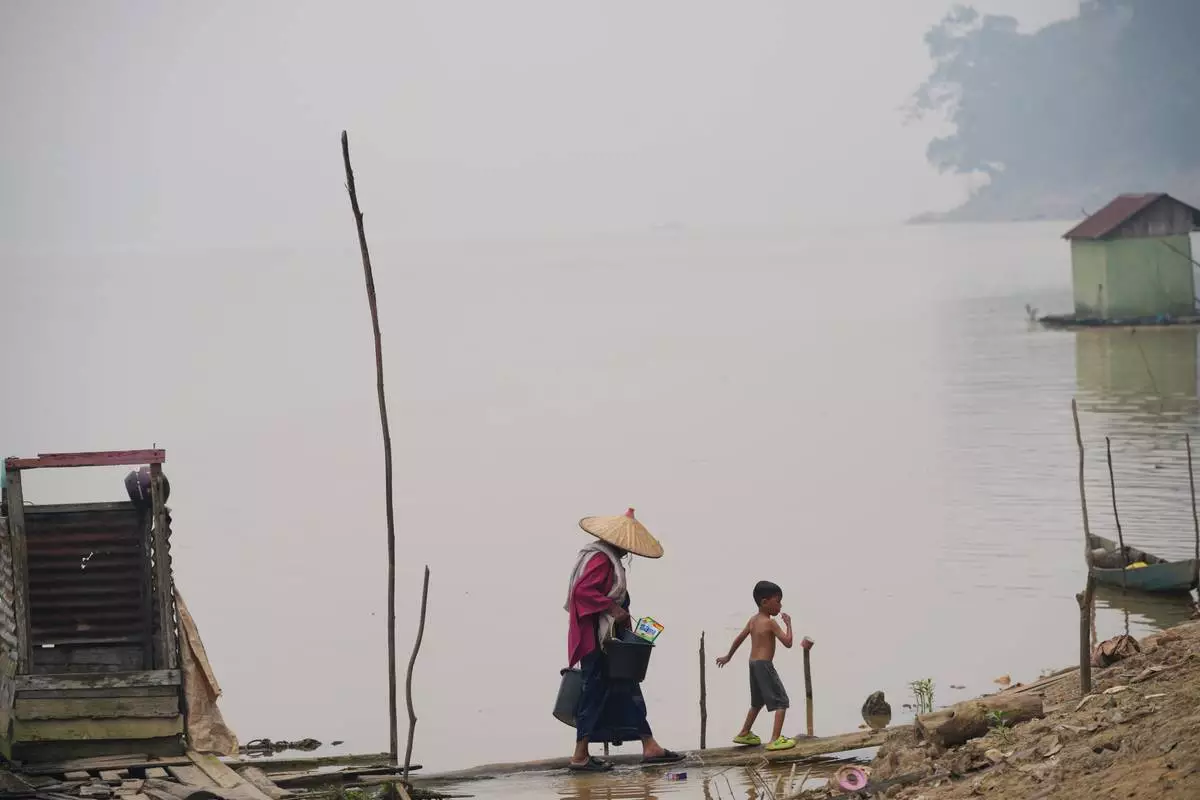 A woman carrying buckets walks with a boy along the Kapuas River amid haze in Sanggau, West Kalimantan, Indonesia, Saturday, Sept. 12, 2026. (AP Photo/Tatan Syuflana)