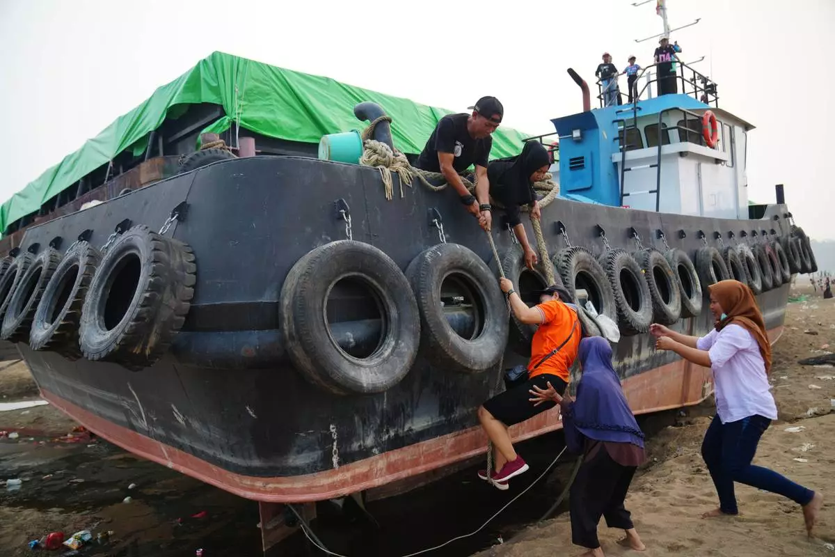 A man helps a woman climb aboard a tugboat grounded on a riverbed of the Kapuas River amid a drought in Sekadau, West Kalimantan, Indonesia, Friday, Sept. 11, 2026. (AP Photo/Tatan Syuflana)