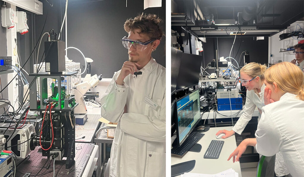 Researchers in safety glasses examine precision laboratory equipment and computer displays in a lab.