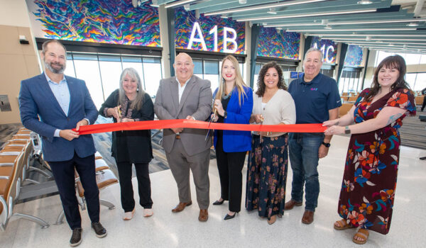 Several individuals hold a red ribbon with scissors as they stand in an airport.