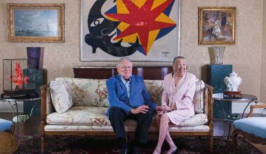 Joe R. and Teresa Lozano Long sit on a couch in front of a colorful painting.