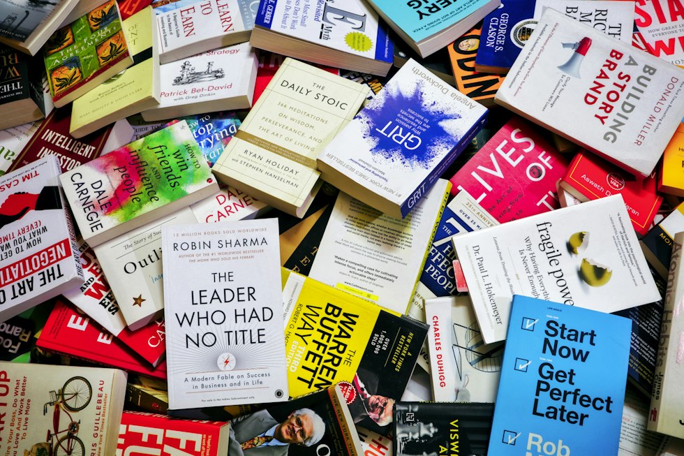 A large pile of various self-help and business books scattered on a surface