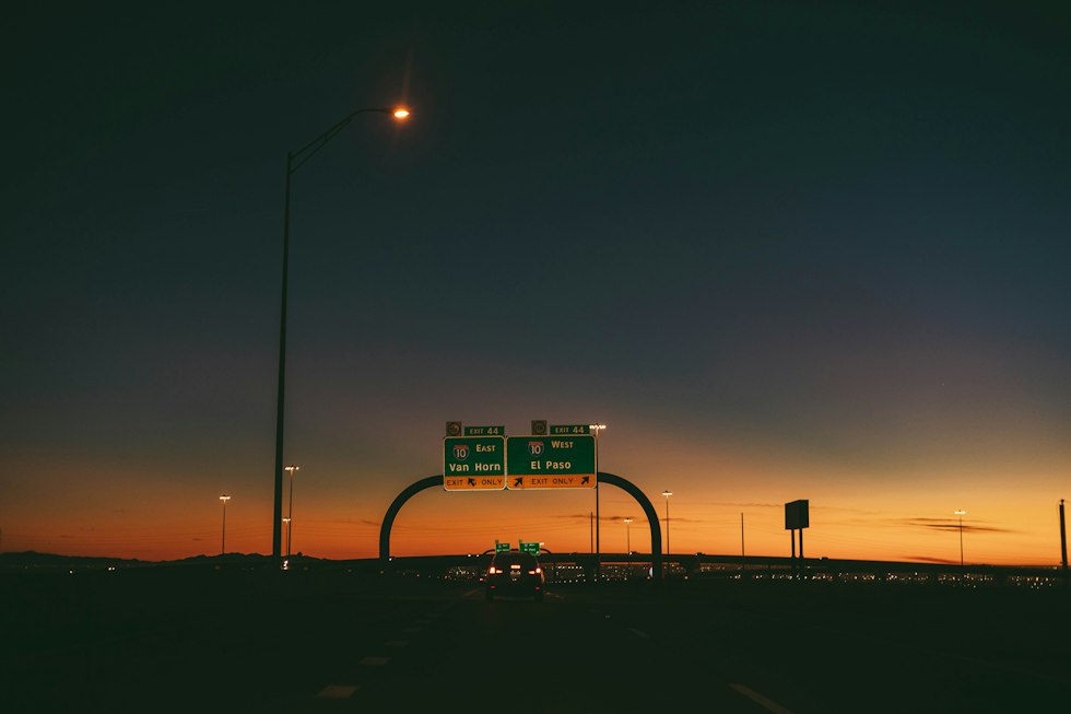 a highway sign at dusk with the sun setting in the background