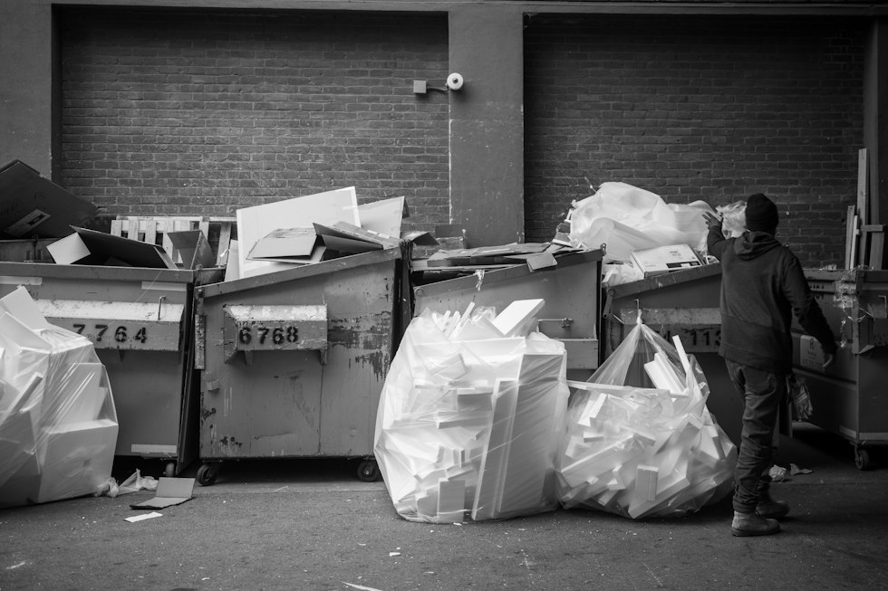 Person standing near dumpsters filled with trash bags