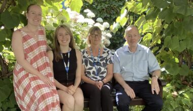 Four people sitting on a bench under a tree, looking at the camera smiling